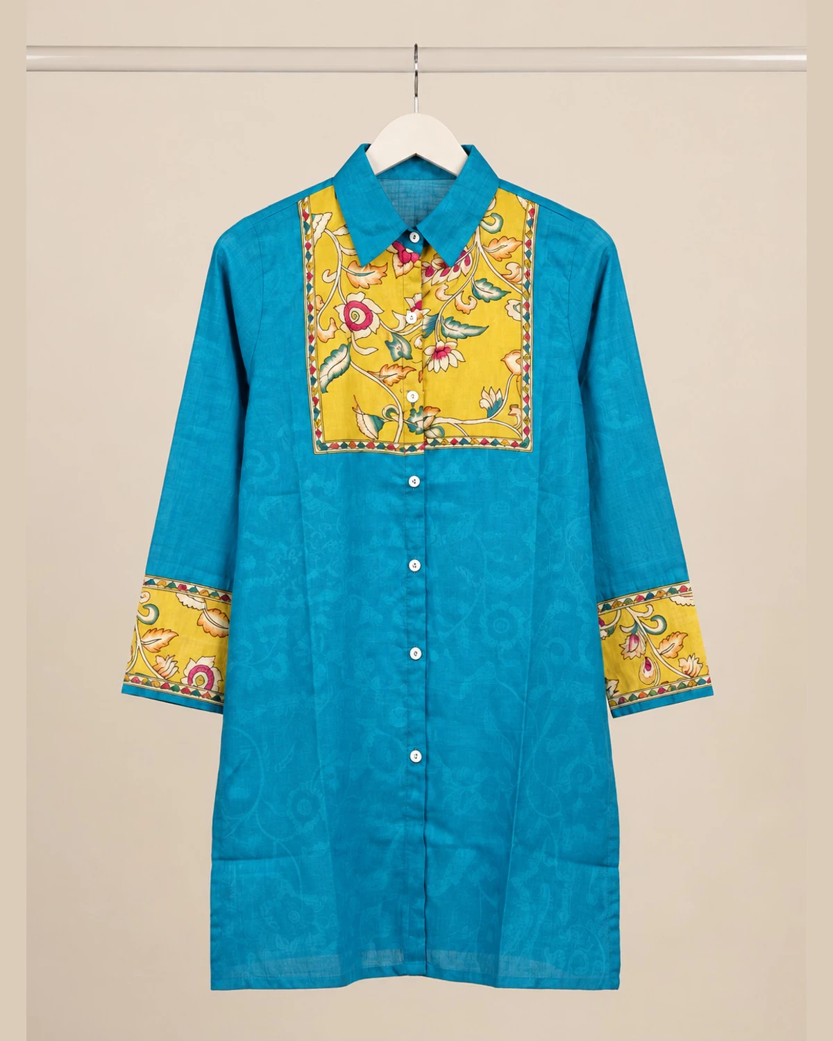 Turquoise cotton shirt kurti with a mustard floral yoke and cuffs on a hanger