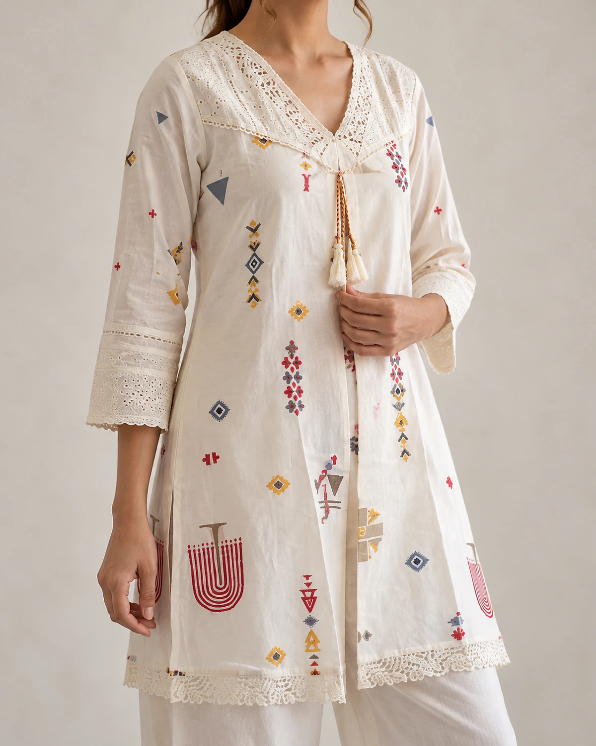 Close-up of the ivory tunic's lace yoke, tassel tie and motifs
