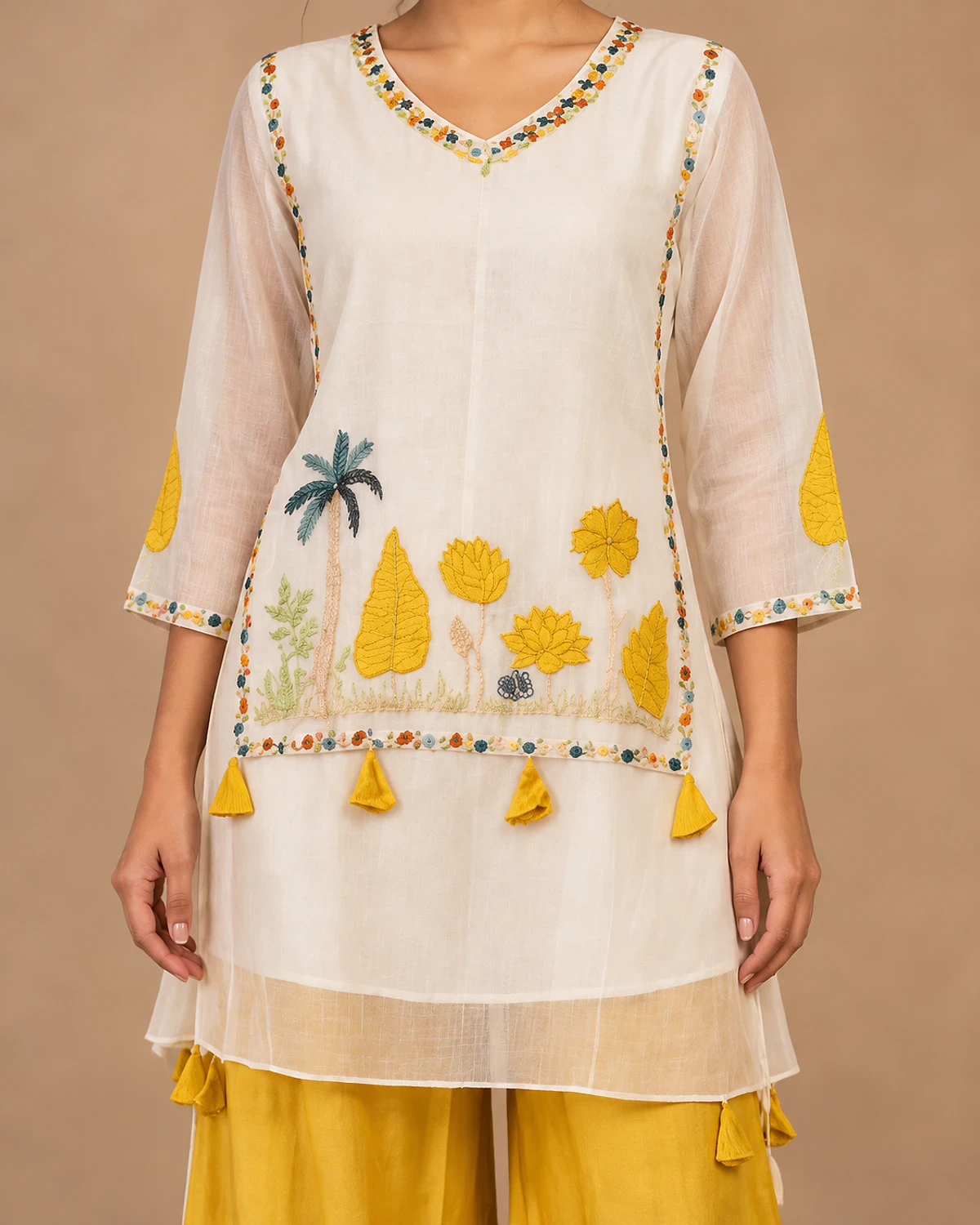 Close-up of the white kurta's yellow embroidered leaf and flower motifs and tassels