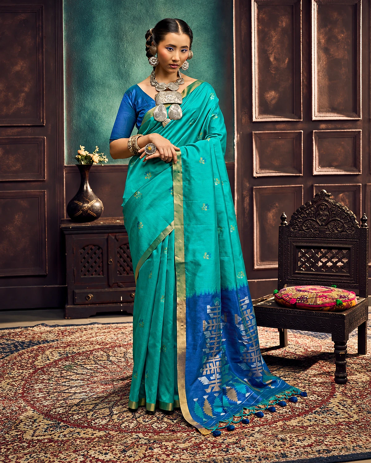 Woman wearing a turquoise Kanoi Paithani tussar silk saree with a gold-tone border and a royal blue geometric pallu with tassels