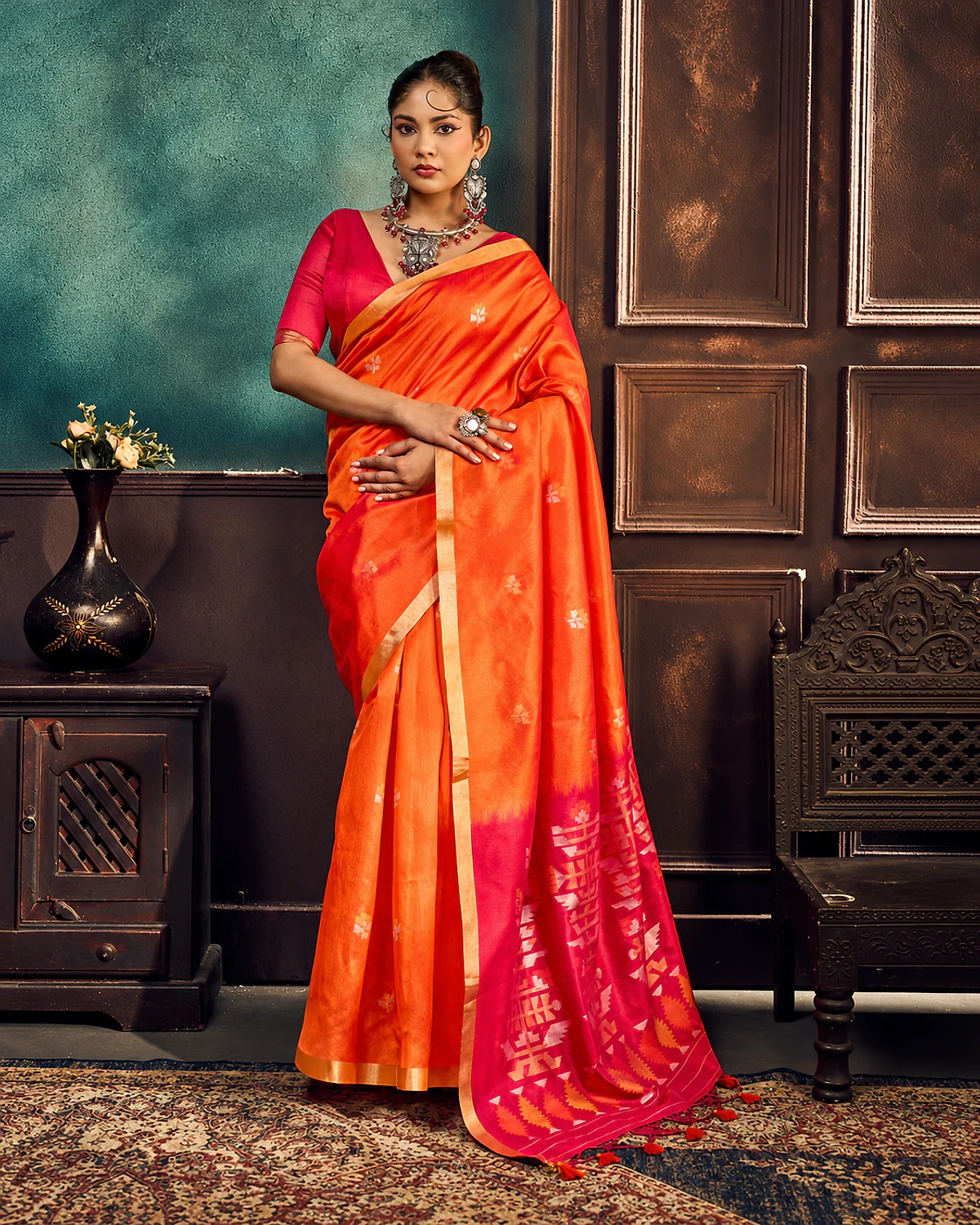 Woman wearing an orange Kanoi Paithani tussar silk saree with a gold-tone border and a pink geometric pallu with tassels
