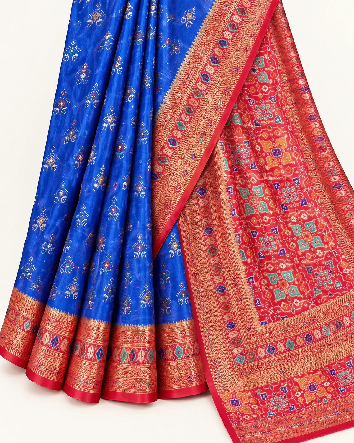 Close-up of the royal blue Tarini saree's folds, red-pink border and Patola-style pallu on a plain background
