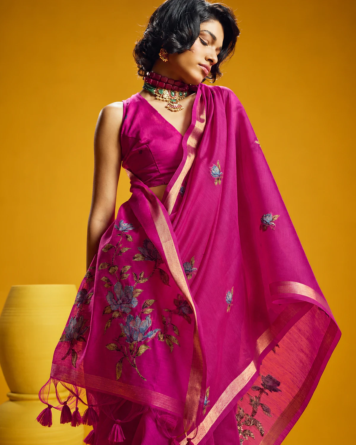 Close-up of the magenta Noorani saree's woven flowers and tasselled pallu, held out by a woman