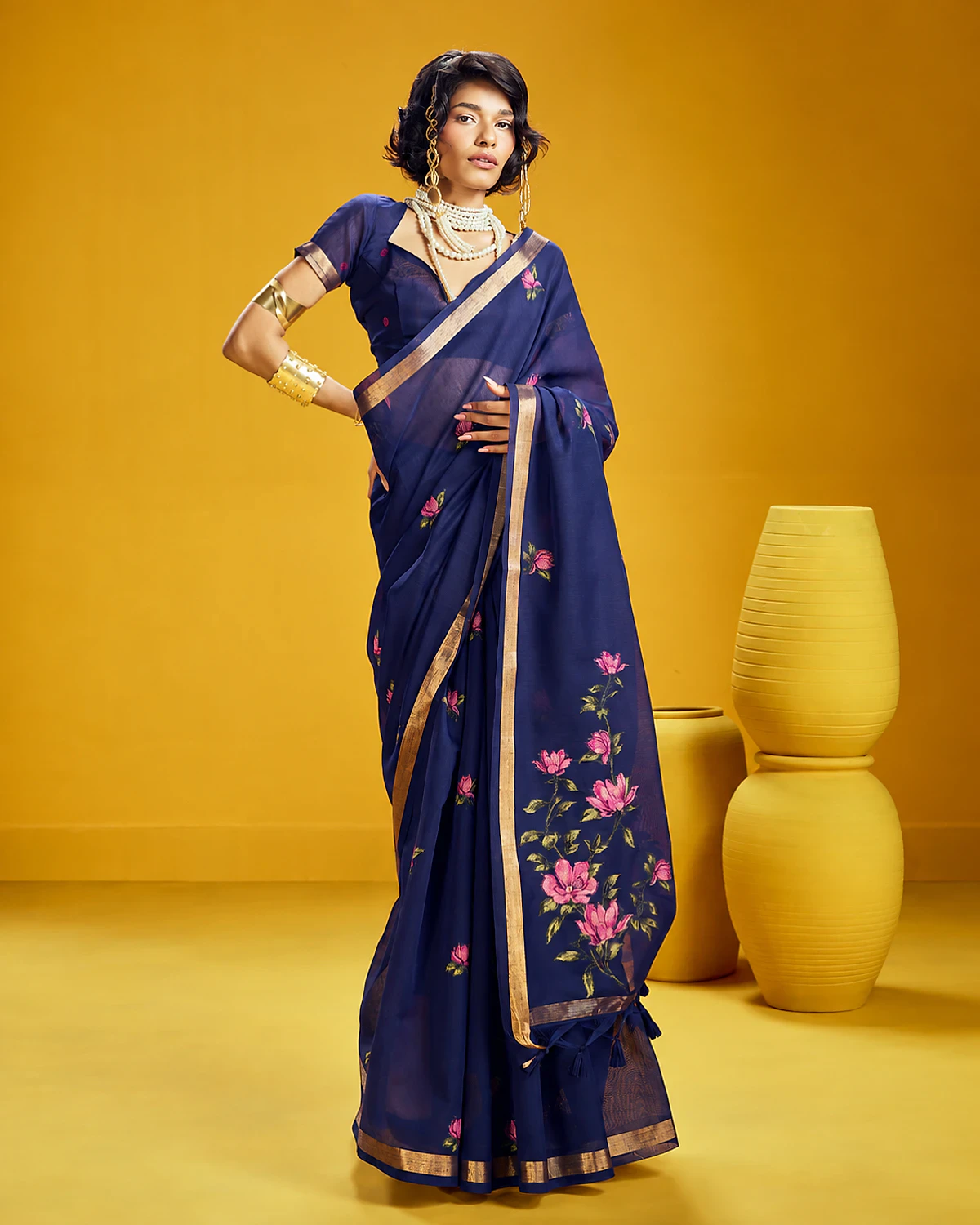 Woman wearing a navy blue Noorani handloom munga cotton saree with woven flowers and a golden border, standing among mustard-yellow pots