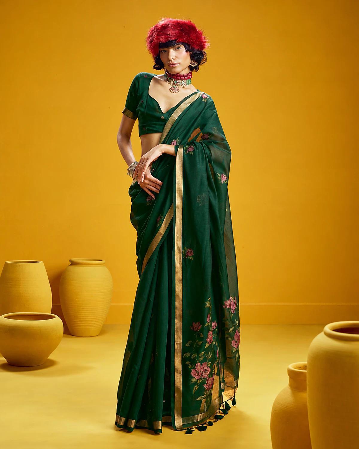 Woman wearing a bottle green Noorani handloom munga cotton saree with woven flowers and a golden border, standing among mustard-yellow pots