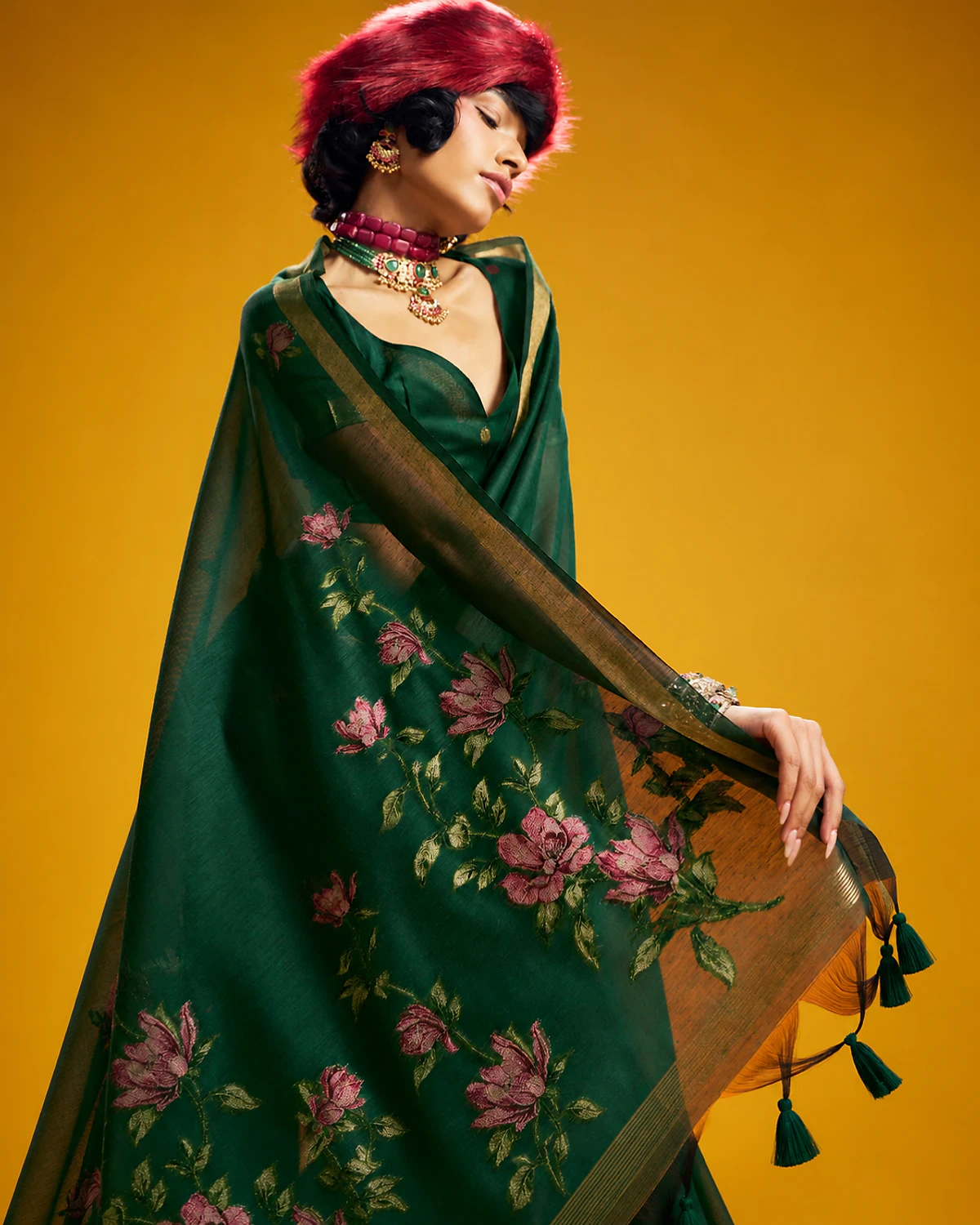 Close-up of the bottle green Noorani saree's woven flowers and tasselled pallu, held out by a woman