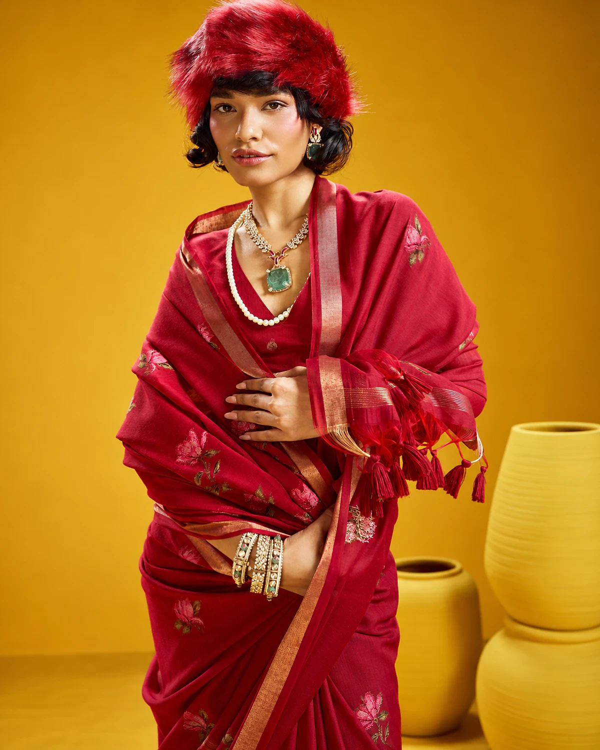 Close-up of the crimson Noorani saree's woven flowers and tasselled pallu, held out by a woman