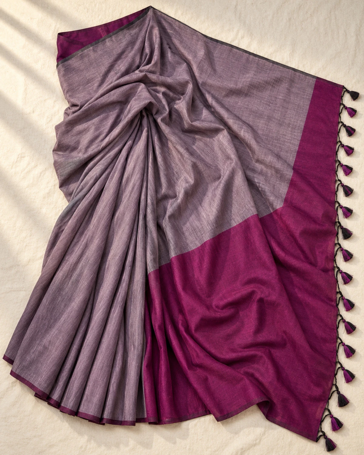 The lilac grey mal cotton saree laid flat, showing its wide purple pallu and tassels