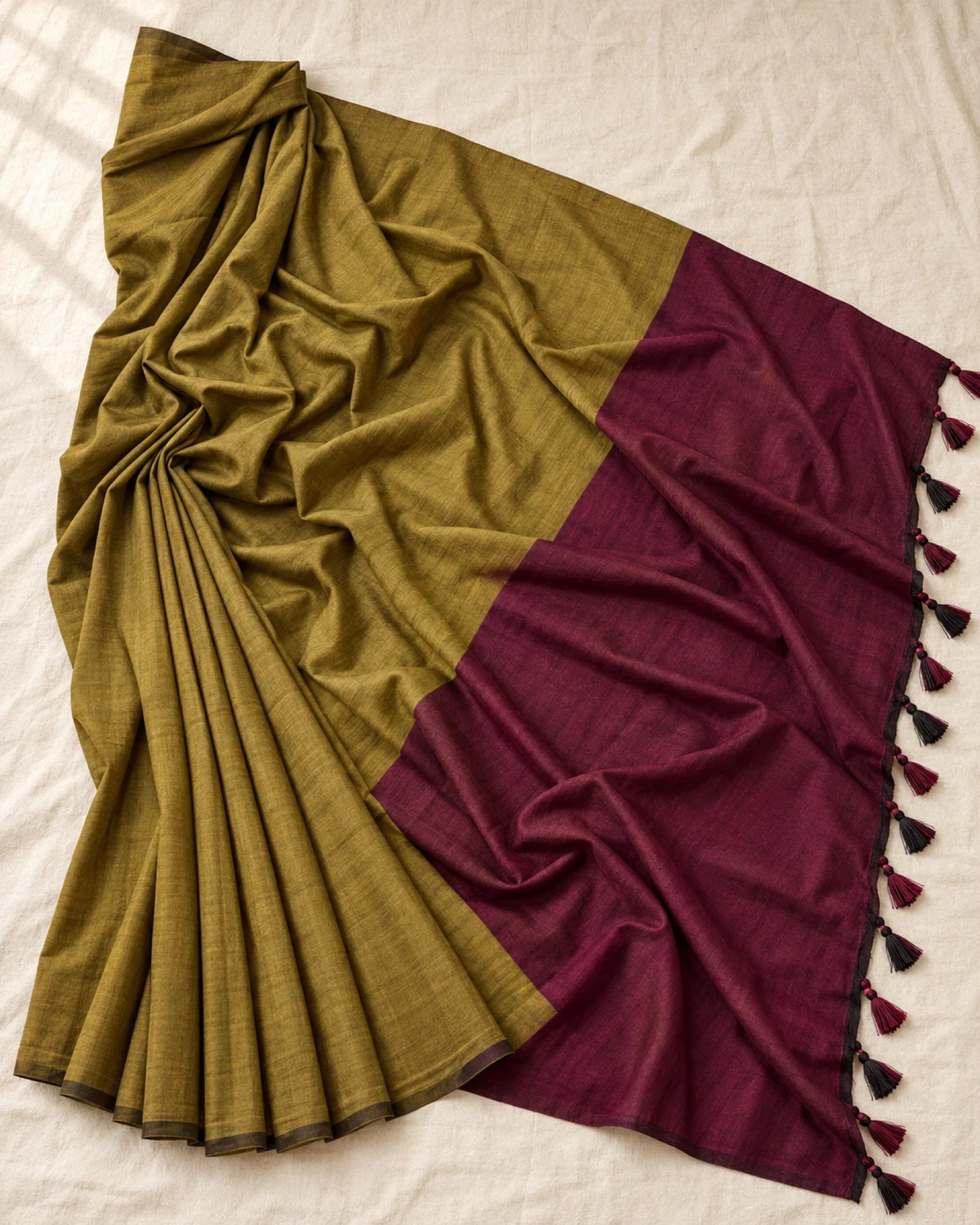 The olive green mal cotton saree laid flat, showing its wide maroon pallu and tassels