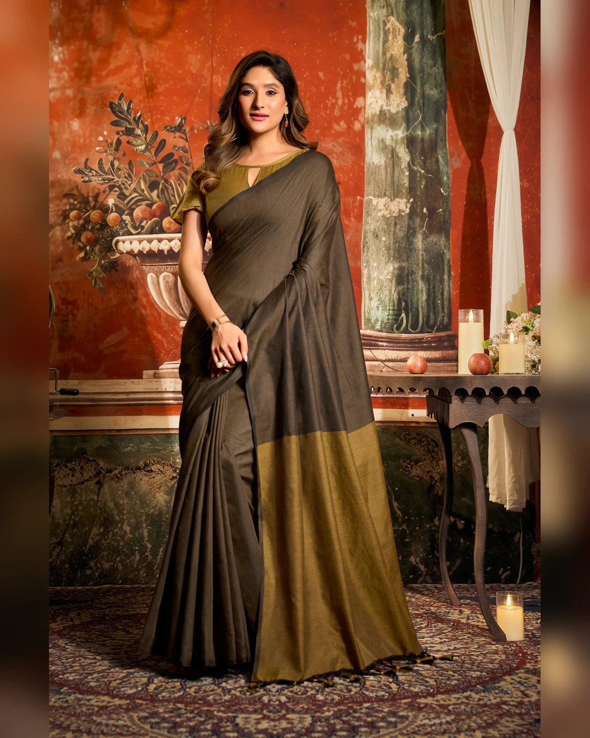 Woman standing in the dark brown mal cotton saree, its wide olive pallu falling in front