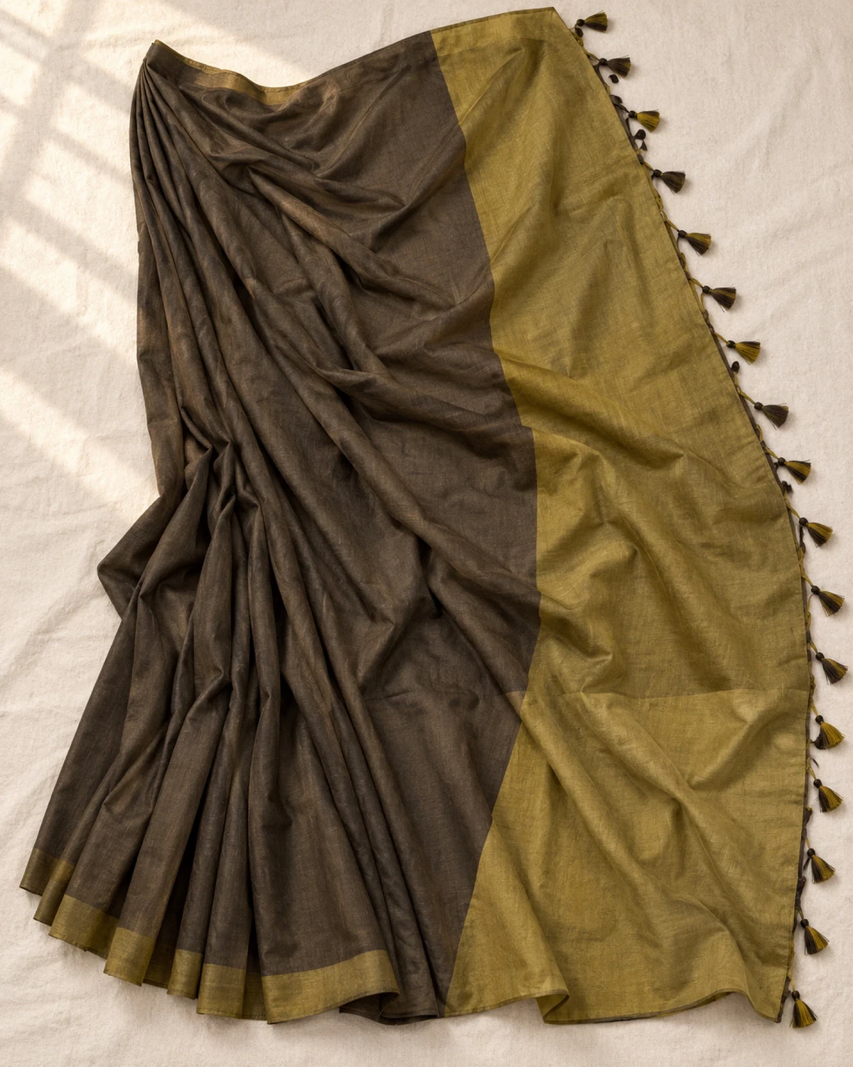 The dark brown mal cotton saree laid flat, showing its wide olive pallu and tassels