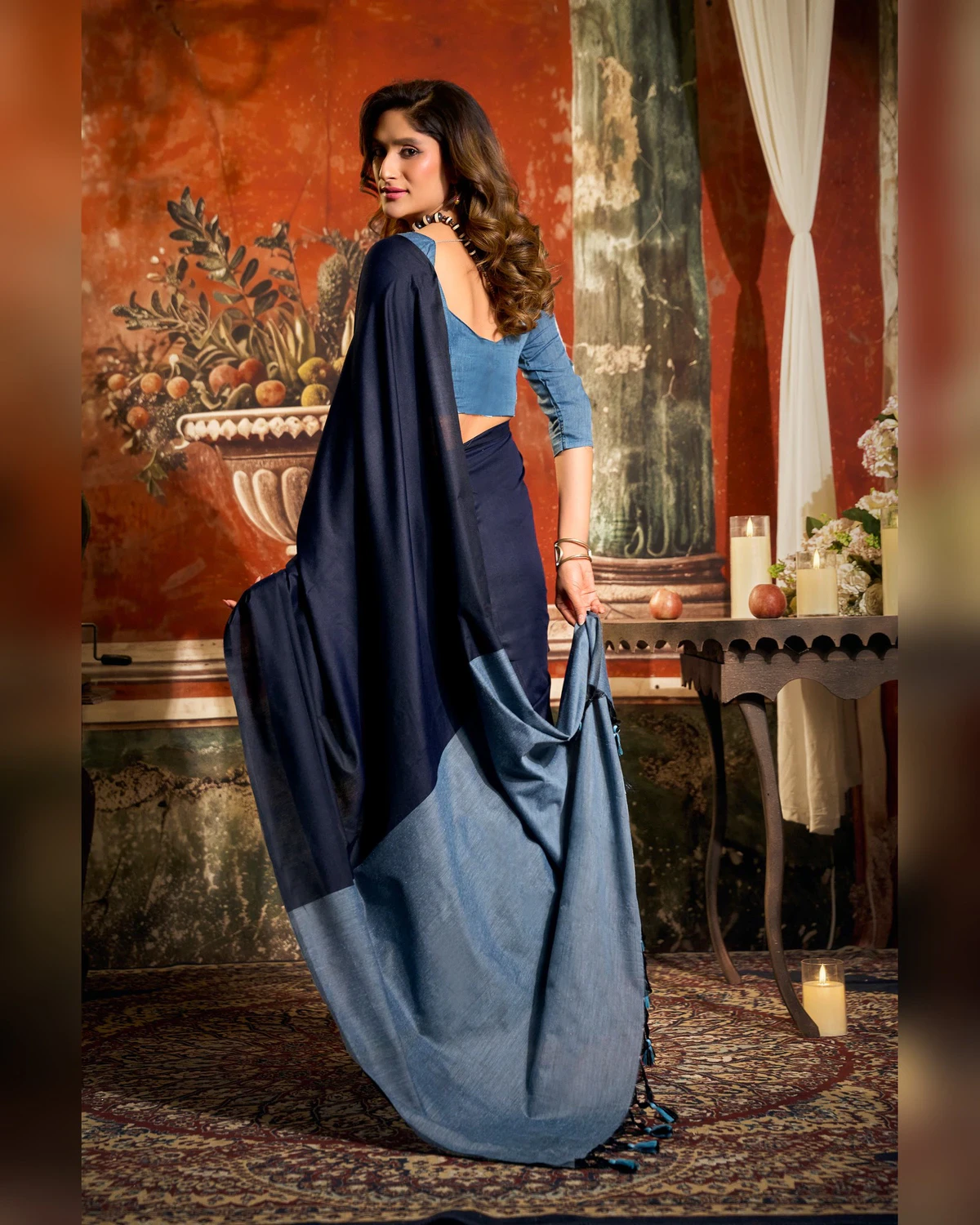 Woman in a navy blue mal cotton saree looking back over her shoulder, holding its powder blue pallu