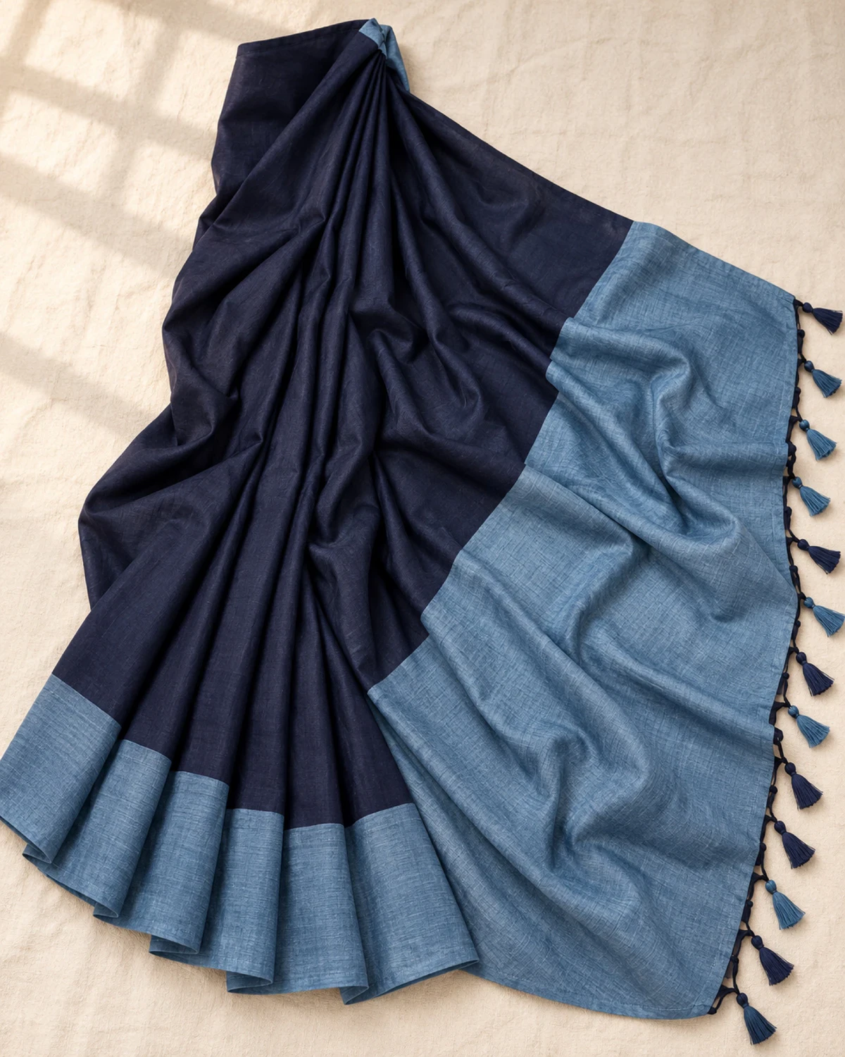 The navy blue mal cotton saree laid flat, showing its powder blue pallu, hem band and tassels