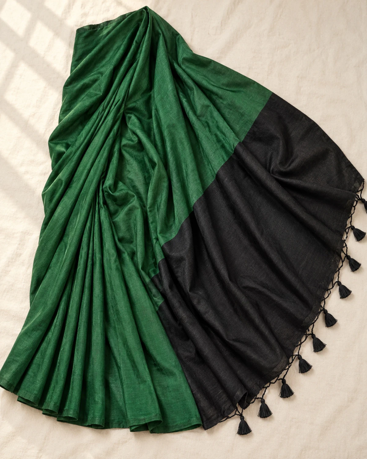 The bottle green mal cotton saree laid flat, showing its wide black pallu and tassels