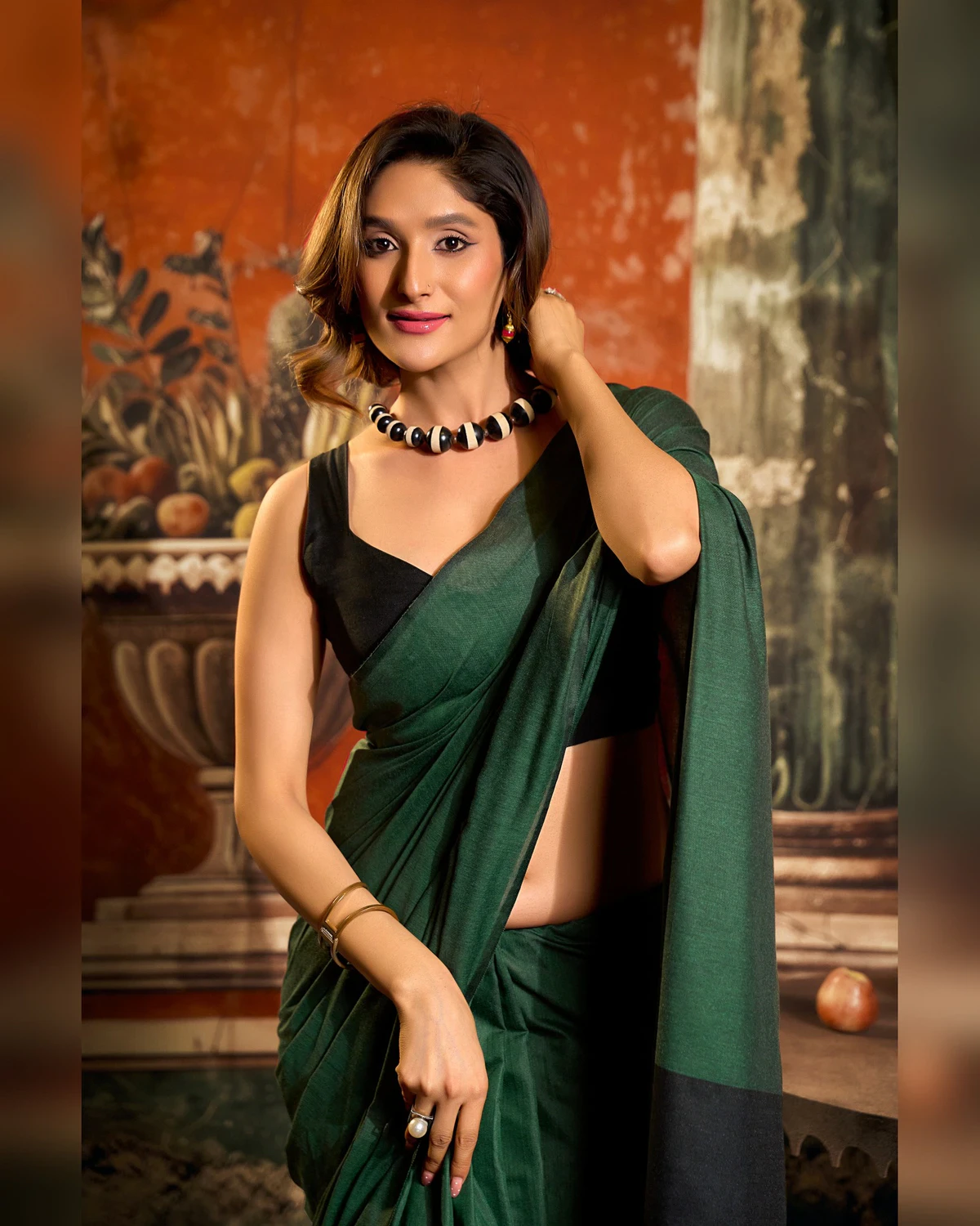 Woman in the bottle green mal cotton saree and a black sleeveless blouse, seen from the waist up