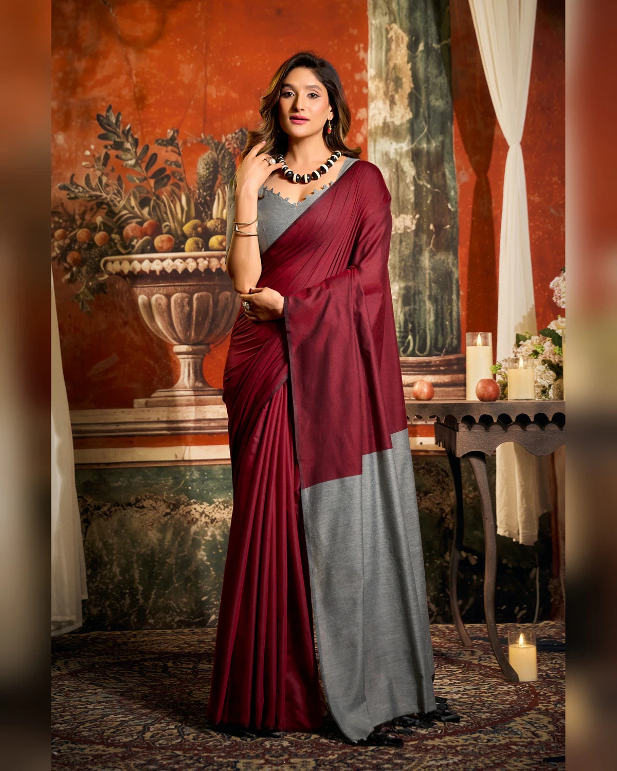 Woman wearing a maroon mal cotton saree with a grey pallu and grey blouse, standing in a room with a painted wall