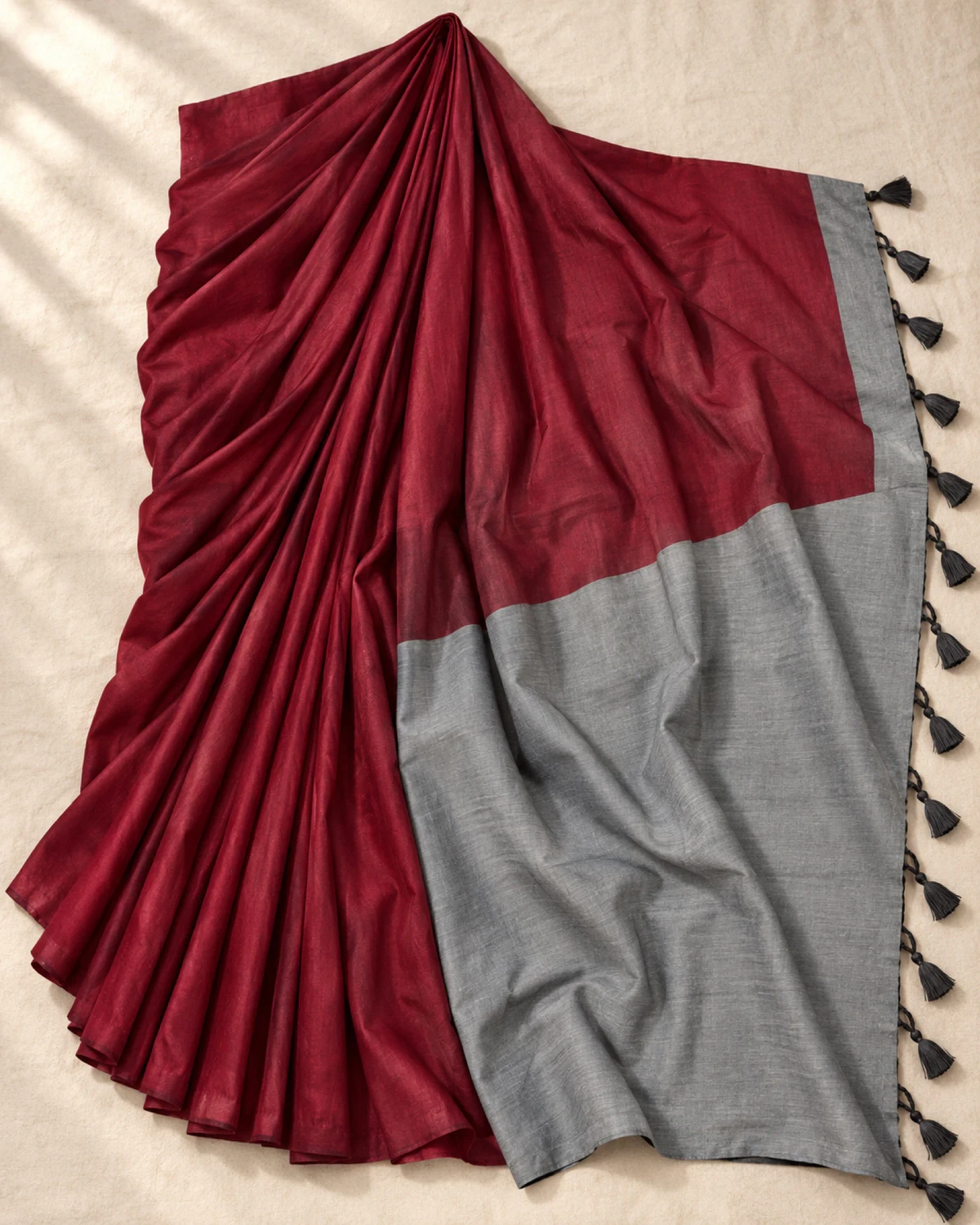 The maroon mal cotton saree laid flat, showing its wide grey pallu and tassels