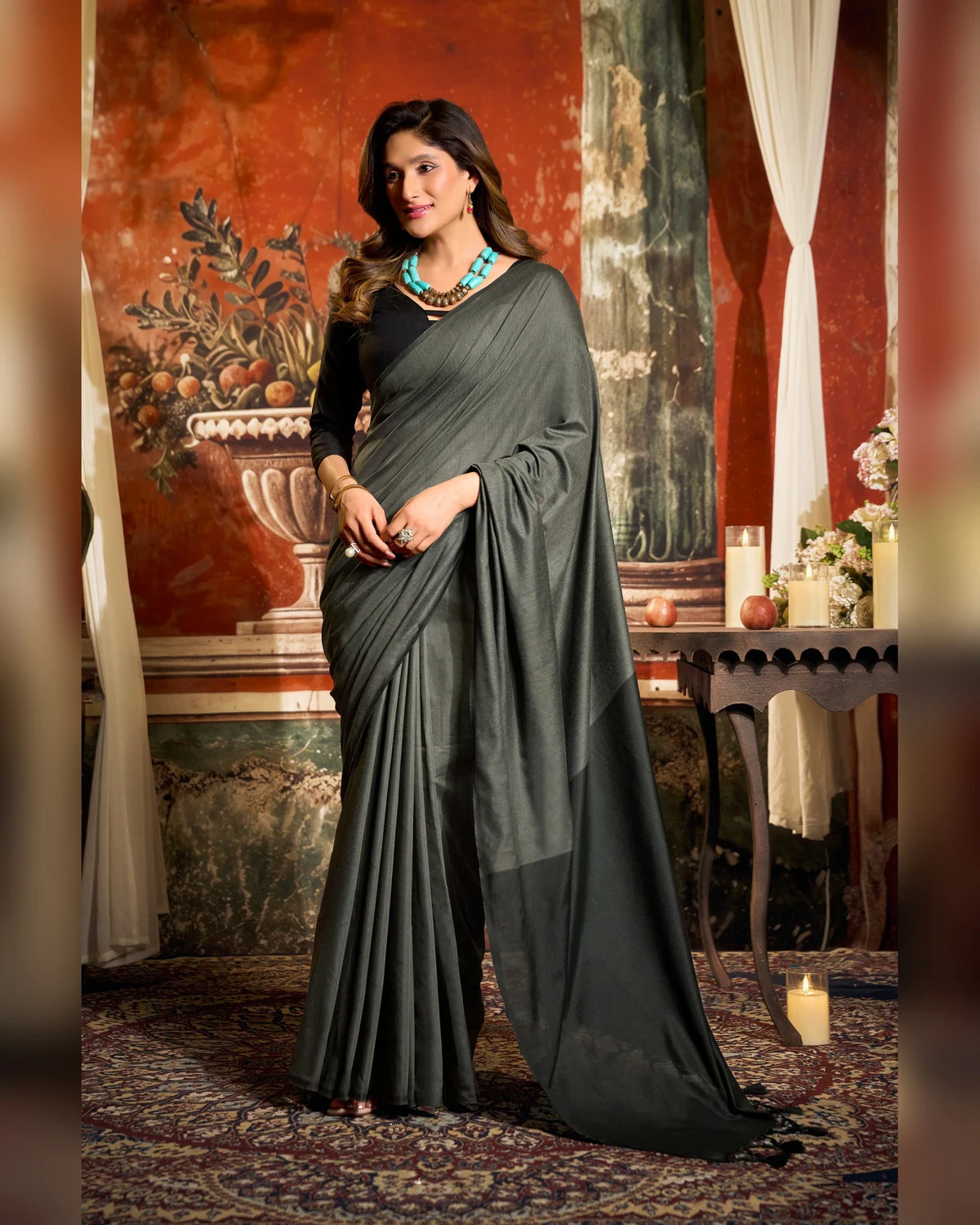 Woman wearing a charcoal grey mal cotton saree with a black blouse and a turquoise necklace, standing in a room with a painted wall