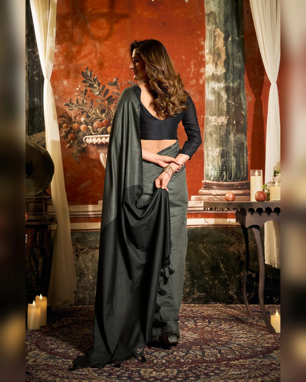 Back view of the charcoal grey mal cotton saree, its pallu held in one hand