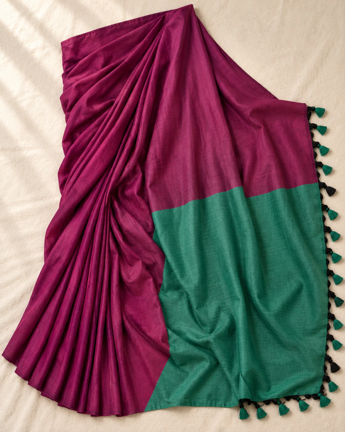 The magenta mal cotton saree laid flat, showing its wide teal-green pallu and tassels
