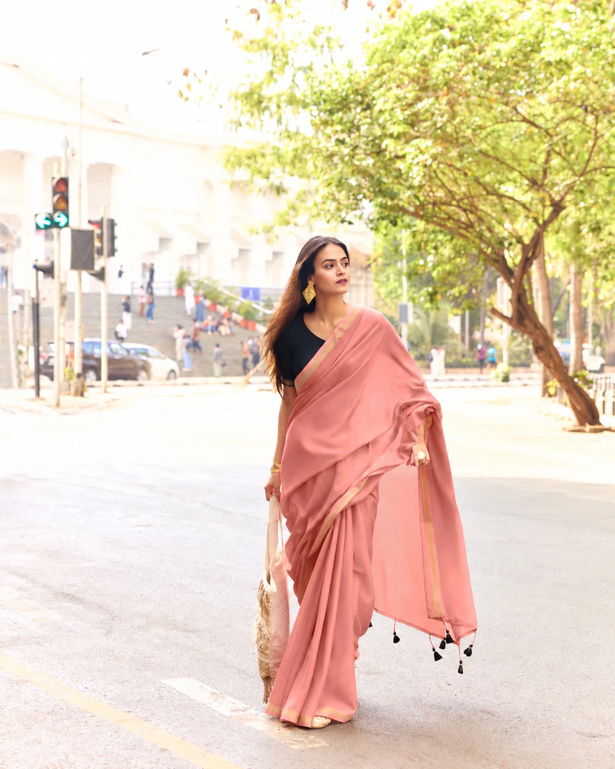 Woman walking down a city street in a dusty pink mul mul cotton saree with a golden border and a black blouse