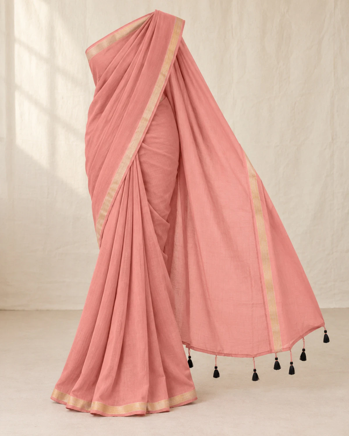 The dusty pink mul mul cotton saree on its own, showing its golden border and black tassels