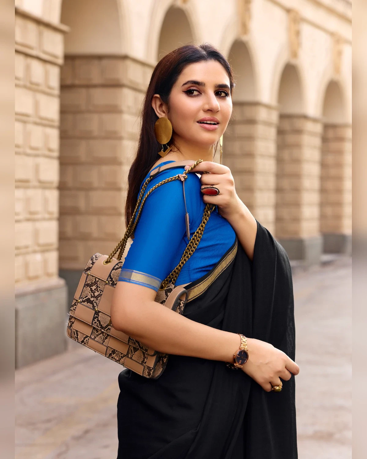 Woman in the black mul mul cotton saree and royal blue blouse with a bag on her shoulder, seen from the waist up