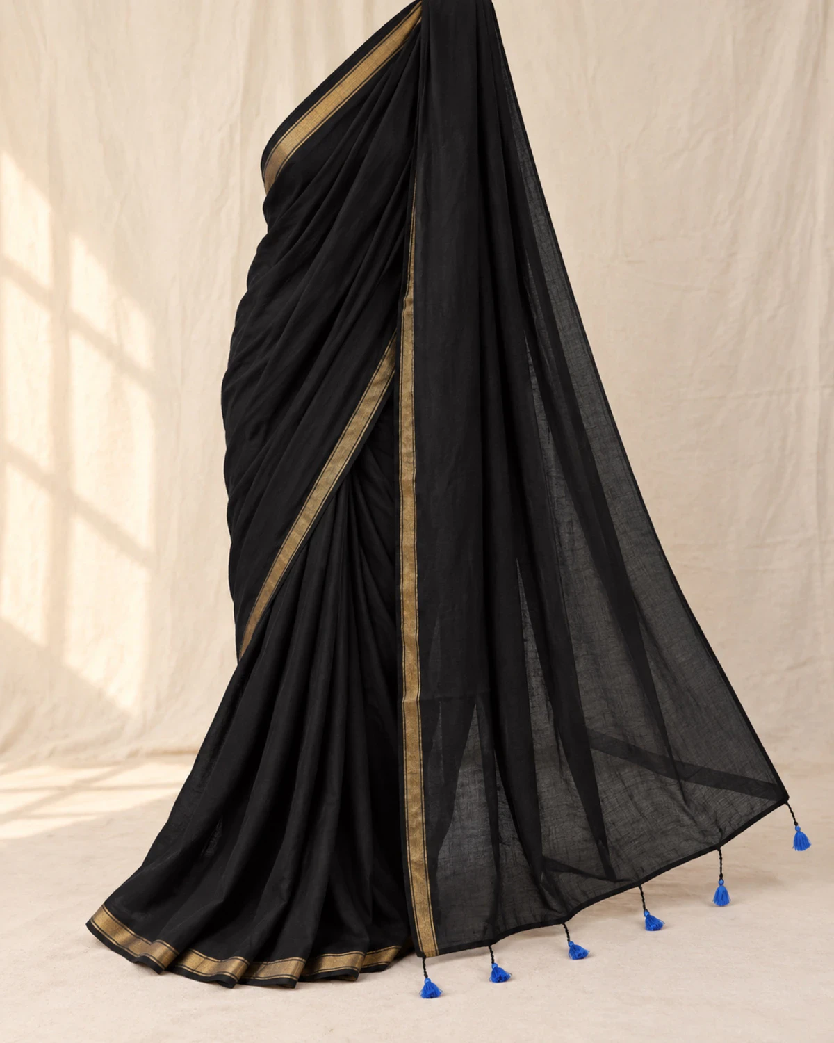 The black mul mul cotton saree on its own, showing its golden border and blue tassels