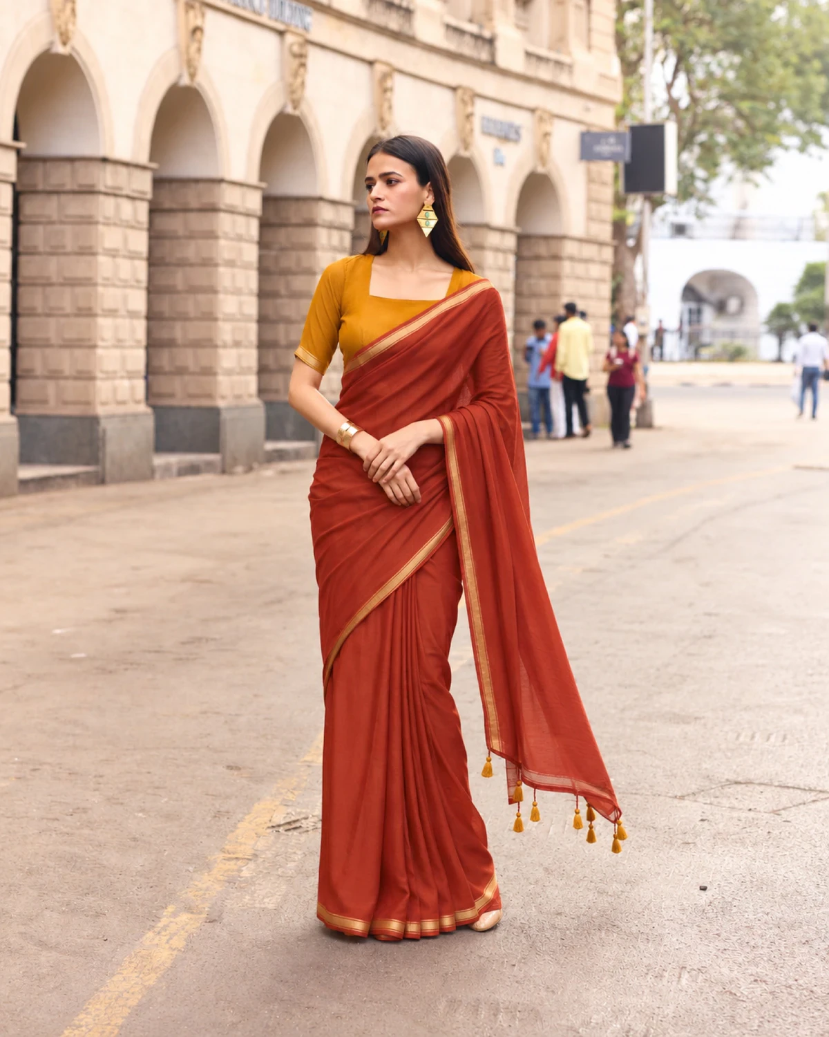 Woman standing in the rust mul mul cotton saree with a golden border, its tasselled pallu over her arm