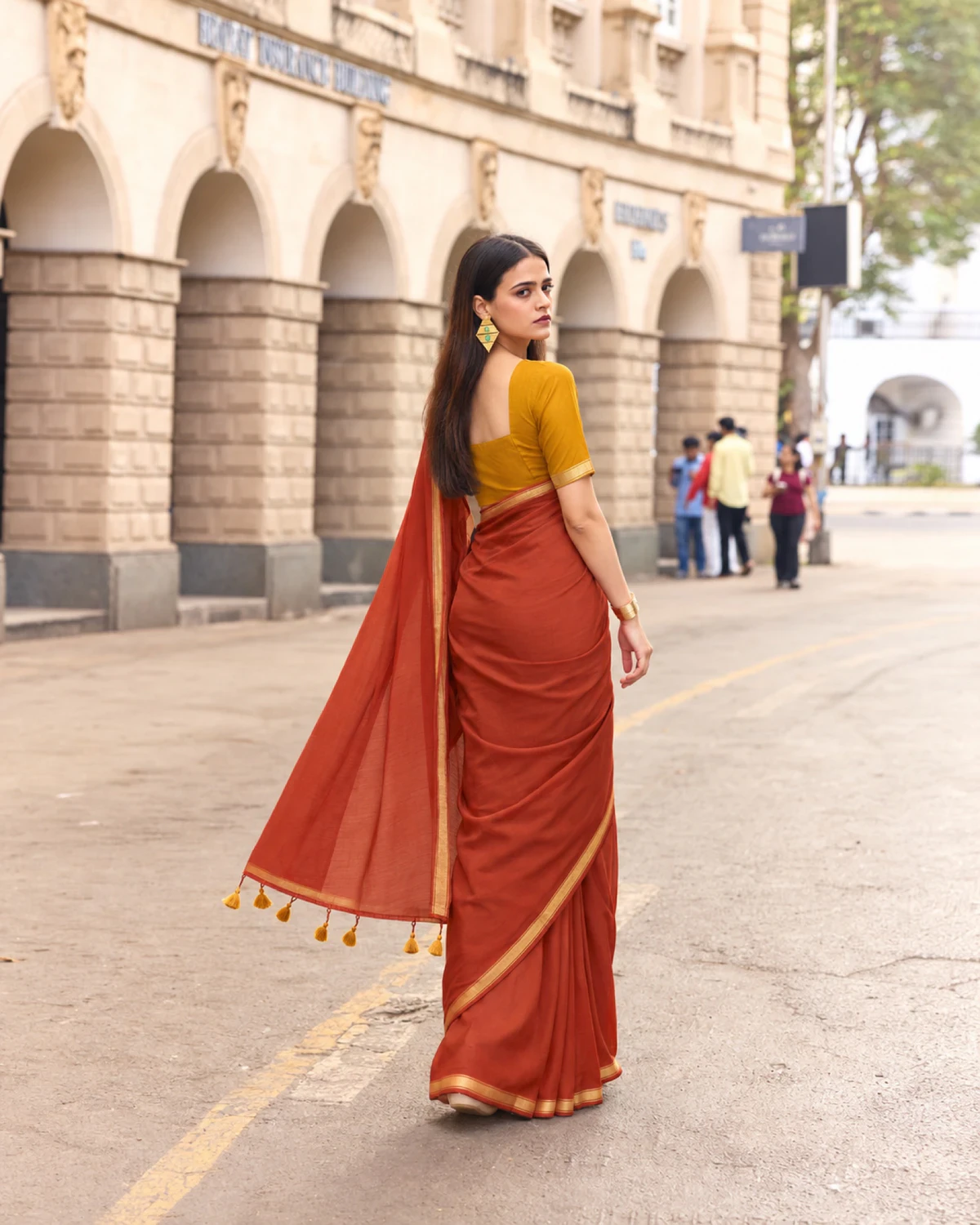 Back view of the rust mul mul cotton saree, its pallu with mustard tassels held out to the side