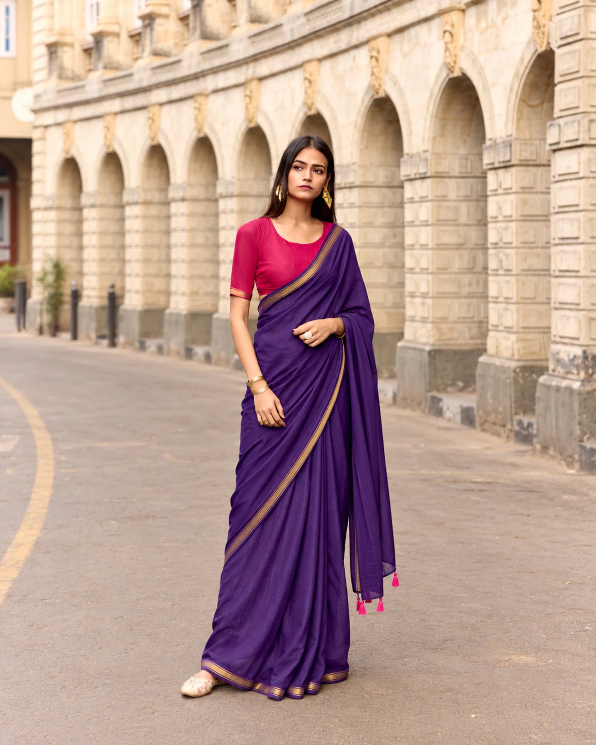 Woman standing in the purple mul mul cotton saree, its pallu with pink tassels over her arm