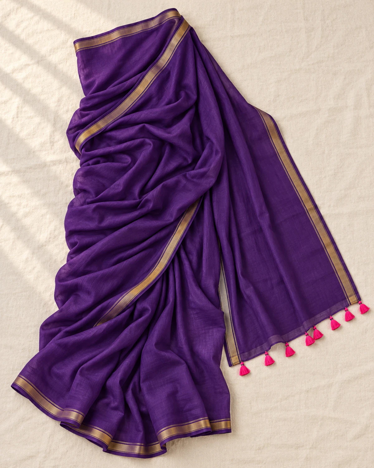The purple mul mul cotton saree laid flat, showing its golden border and pink tassels