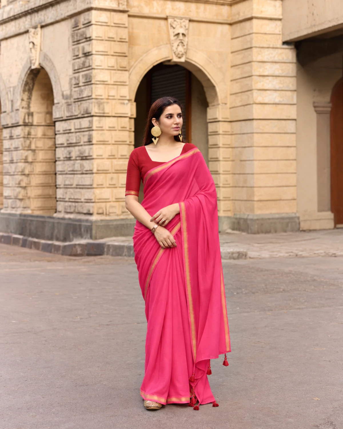 Woman standing in the rani pink mul mul cotton saree, its pallu with red tassels over her arm