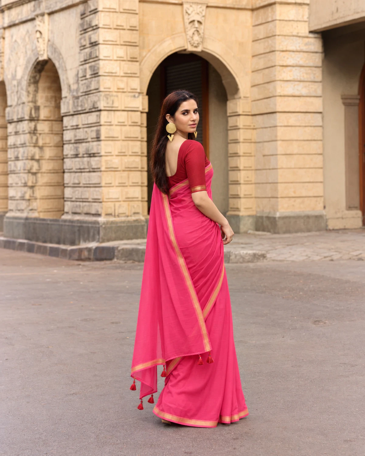 Back view of the rani pink mul mul cotton saree, its pallu with red tassels held out to the side