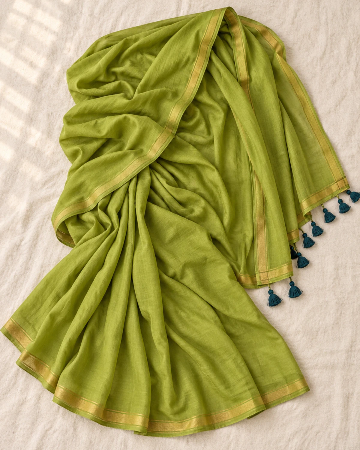 The olive green mul mul cotton saree laid flat, showing its golden border and teal tassels