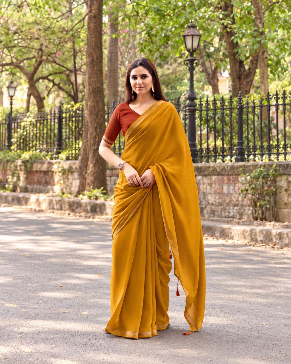 Woman standing in the mustard yellow mul mul cotton saree on a tree-lined street, its pallu over her arm