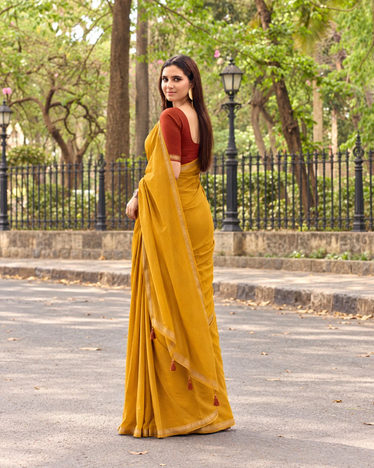 Back view of the mustard yellow mul mul cotton saree, its pallu with rust tassels falling down the back
