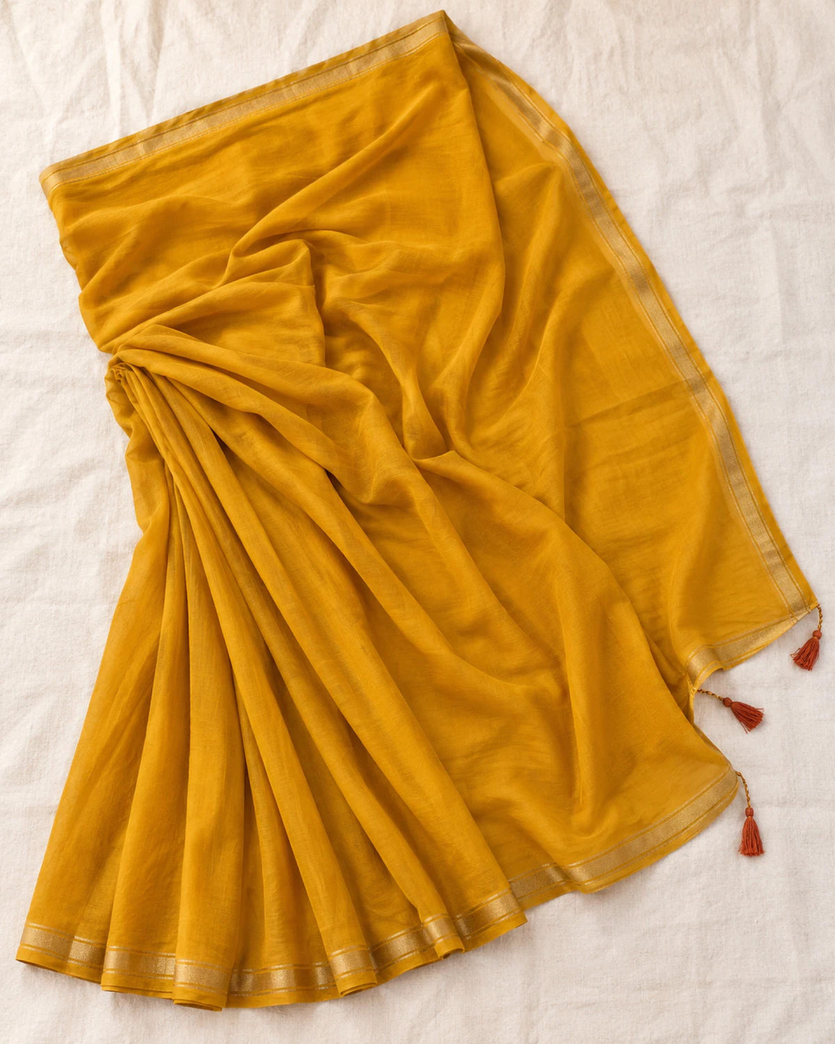 The mustard yellow mul mul cotton saree laid flat, showing its golden border and rust tassels