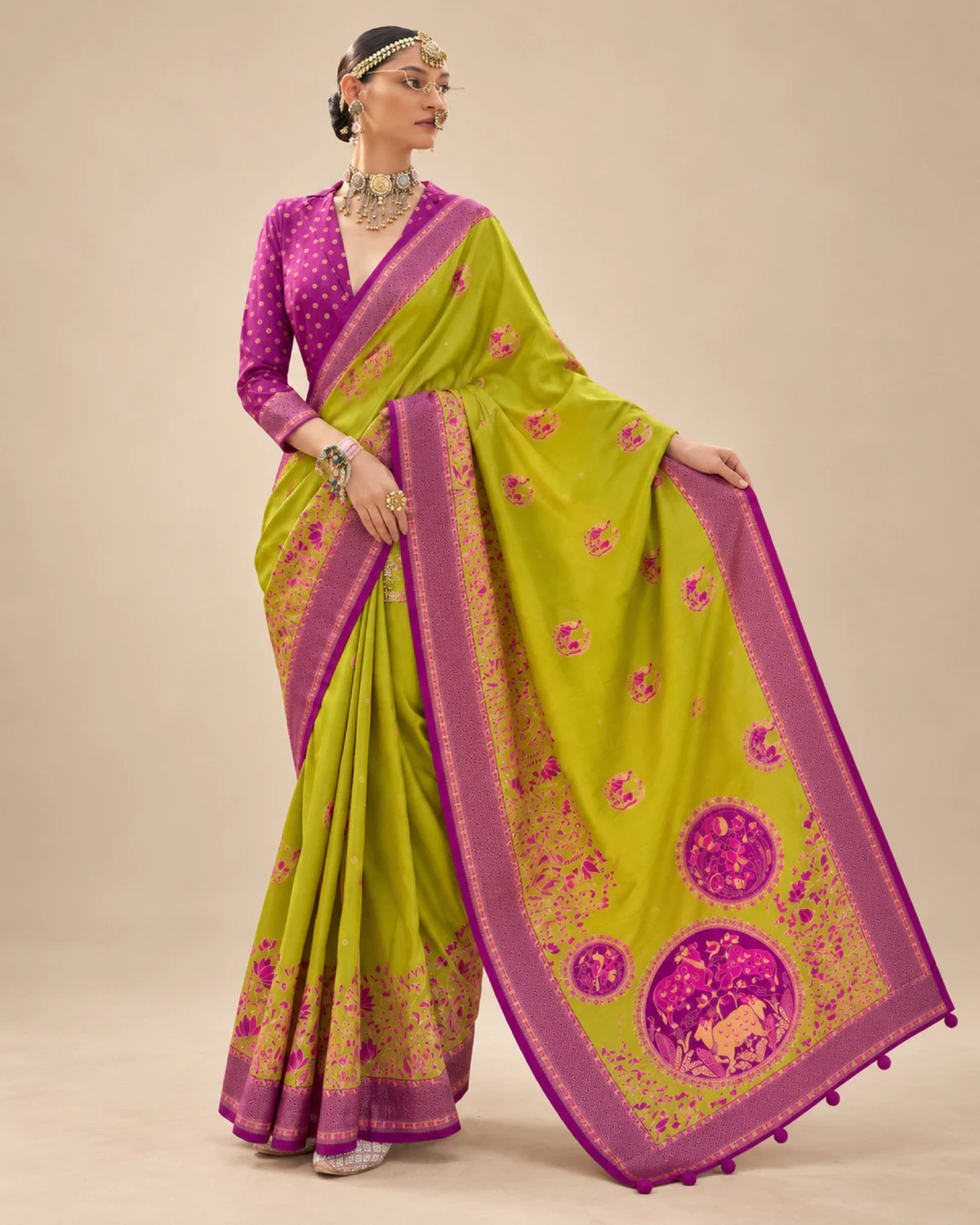 Woman holding out the lime green saree's pallu to show its large medallions and pom-pom tassels