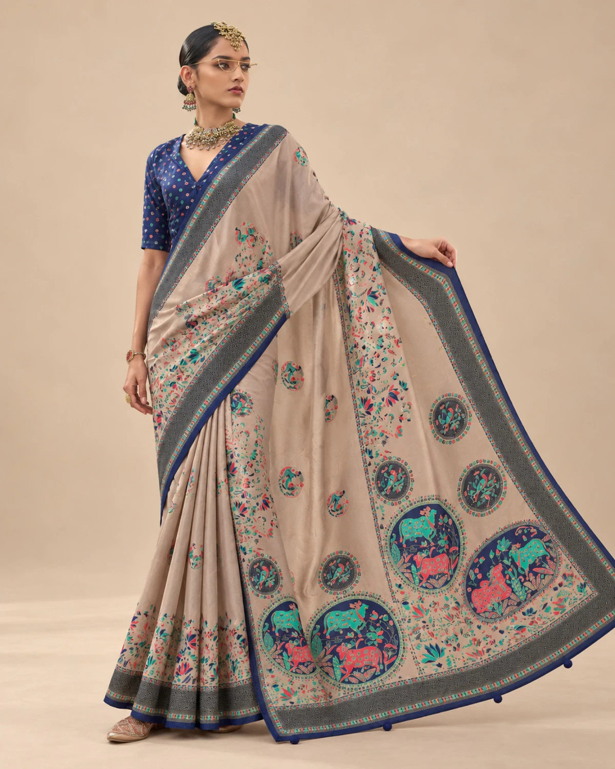 Woman holding out the beige saree's pallu to show its large medallions and pom-pom tassels