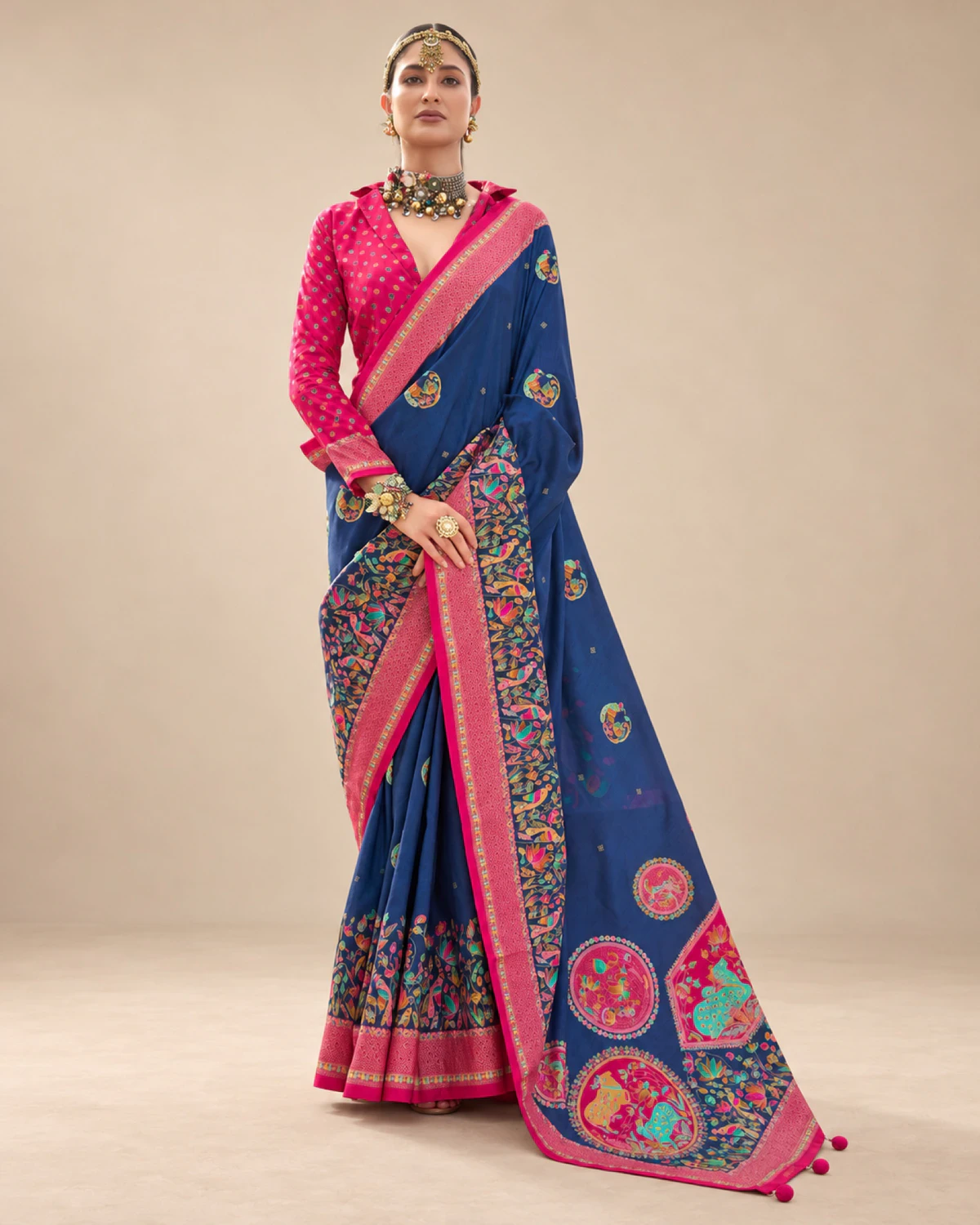 Woman wearing a navy blue printed sigma silk saree with a rani pink border and medallion pallu, standing against a beige wall