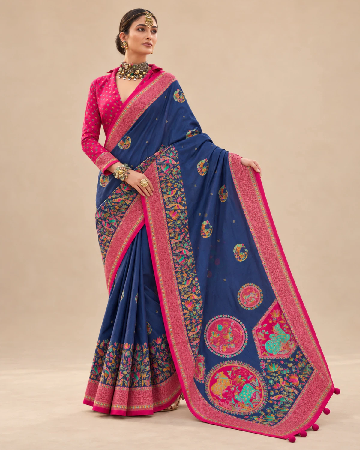 Woman holding out the navy blue saree's pallu to show its large medallions and pom-pom tassels