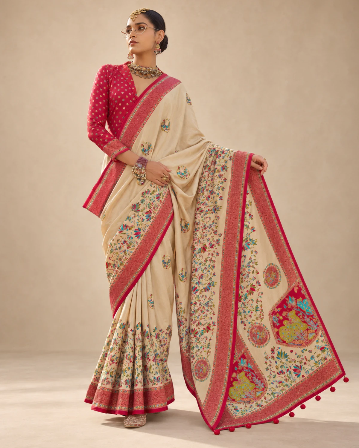 Woman holding out the cream saree's pallu to show its large medallions and pom-pom tassels