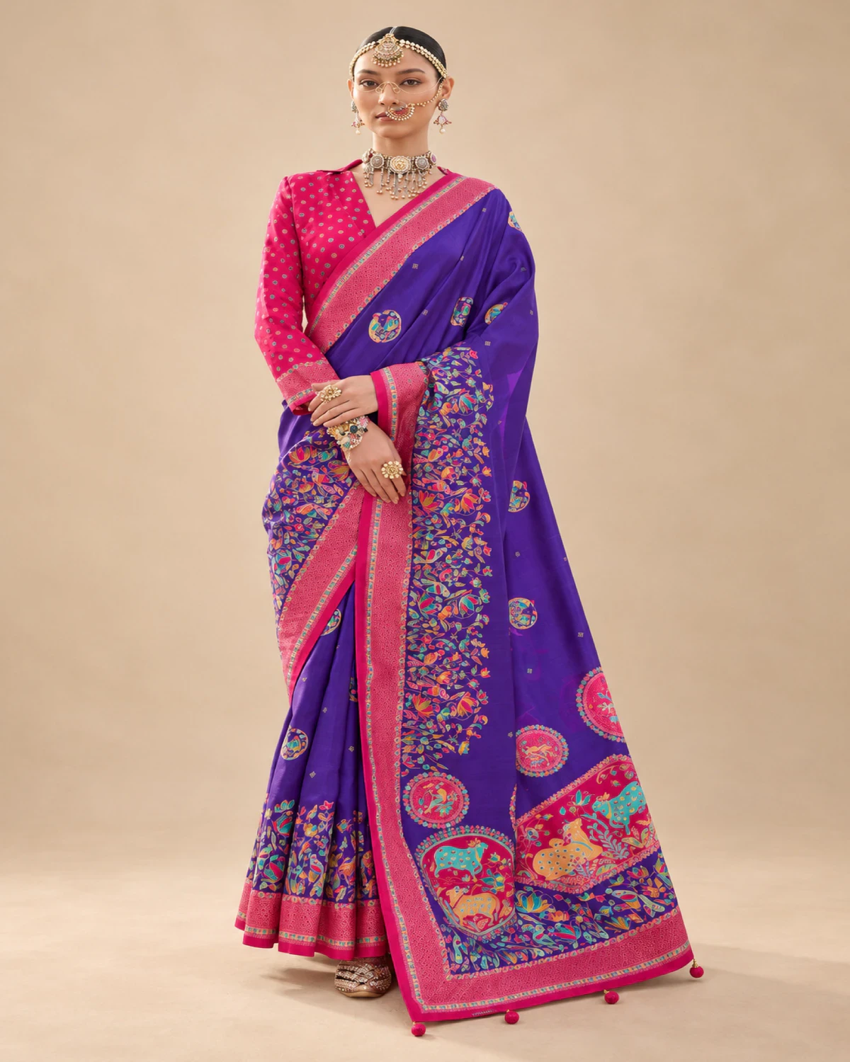 Woman wearing a purple printed sigma silk saree with a rani pink border and medallion pallu, standing against a beige wall