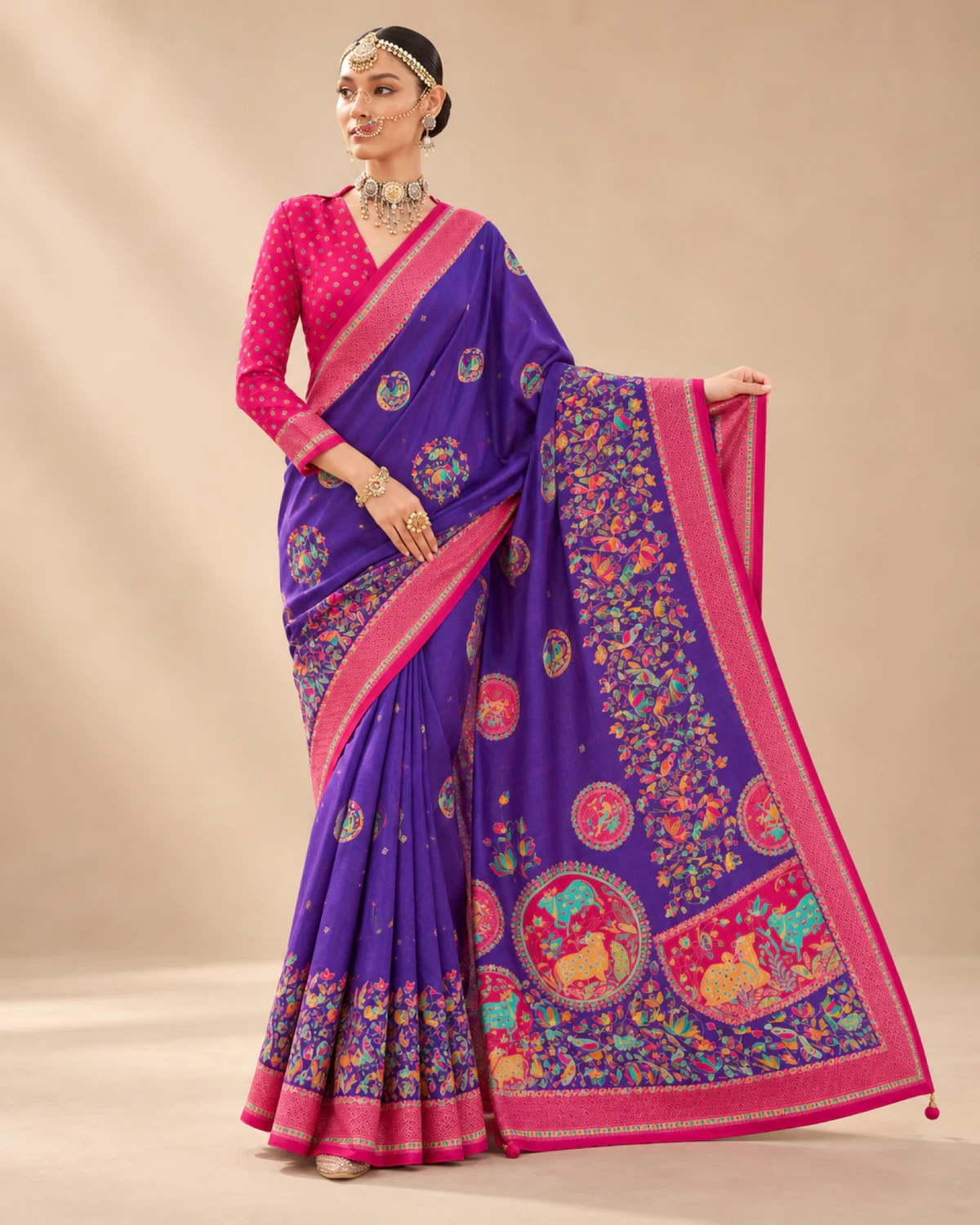 Woman holding out the purple saree's pallu to show its large medallions and pom-pom tassels