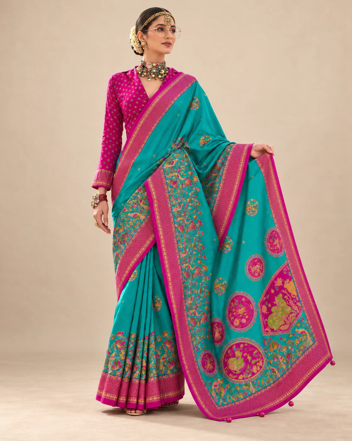 Woman holding out the teal saree's pallu to show its large medallions and pom-pom tassels