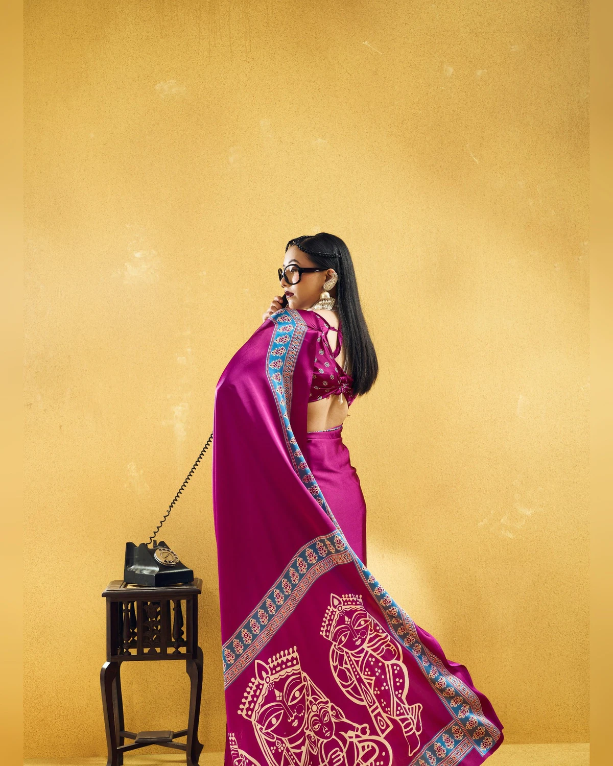 Woman in the rani pink modal satin saree seen from the back, its pallu of cream figures falling behind her