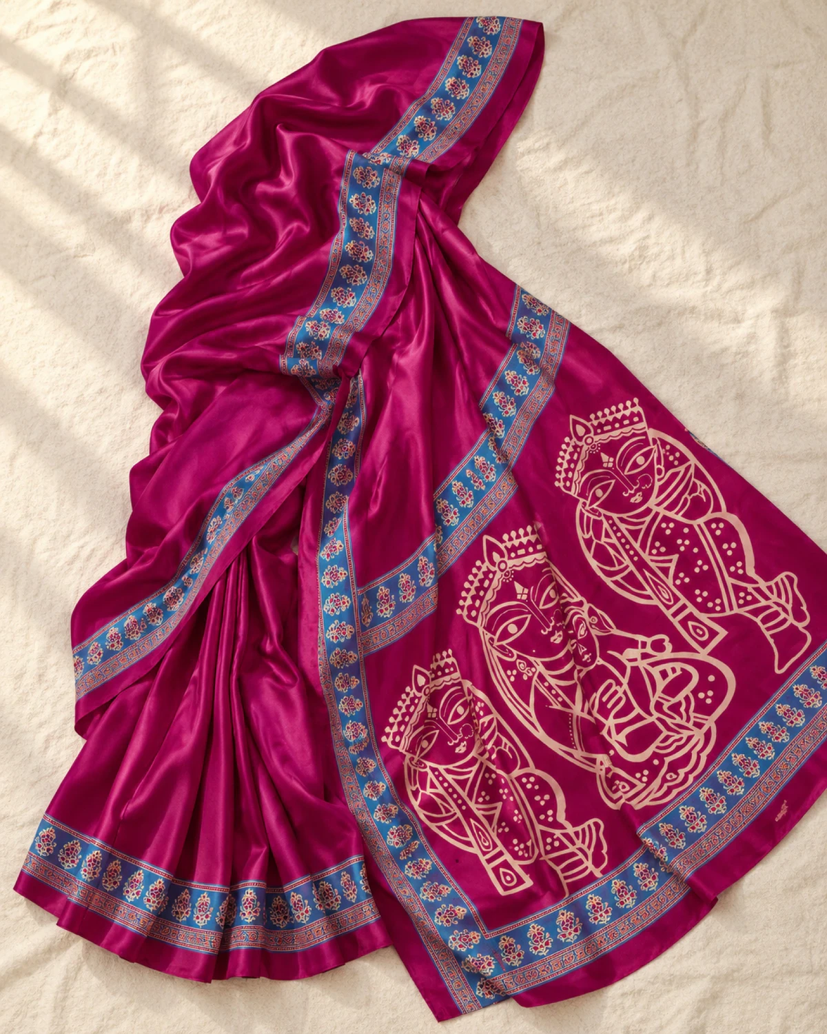 The rani pink modal satin saree laid out flat, showing its blue Ajrakh border and figure pallu