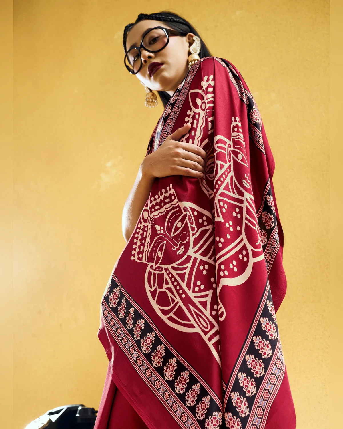 Close view of the red modal satin saree's pallu over a woman's shoulder, with cream figures and a black Ajrakh border