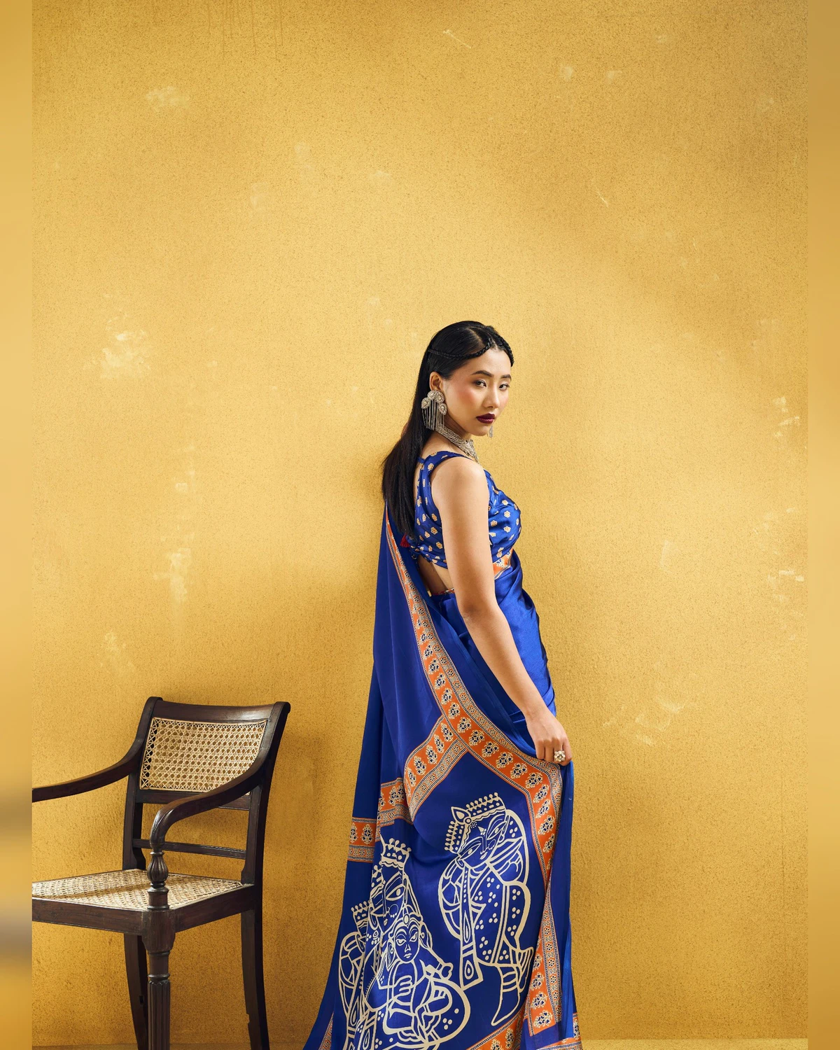Woman in the royal blue modal satin saree seen from the side, its pallu of cream figures behind her